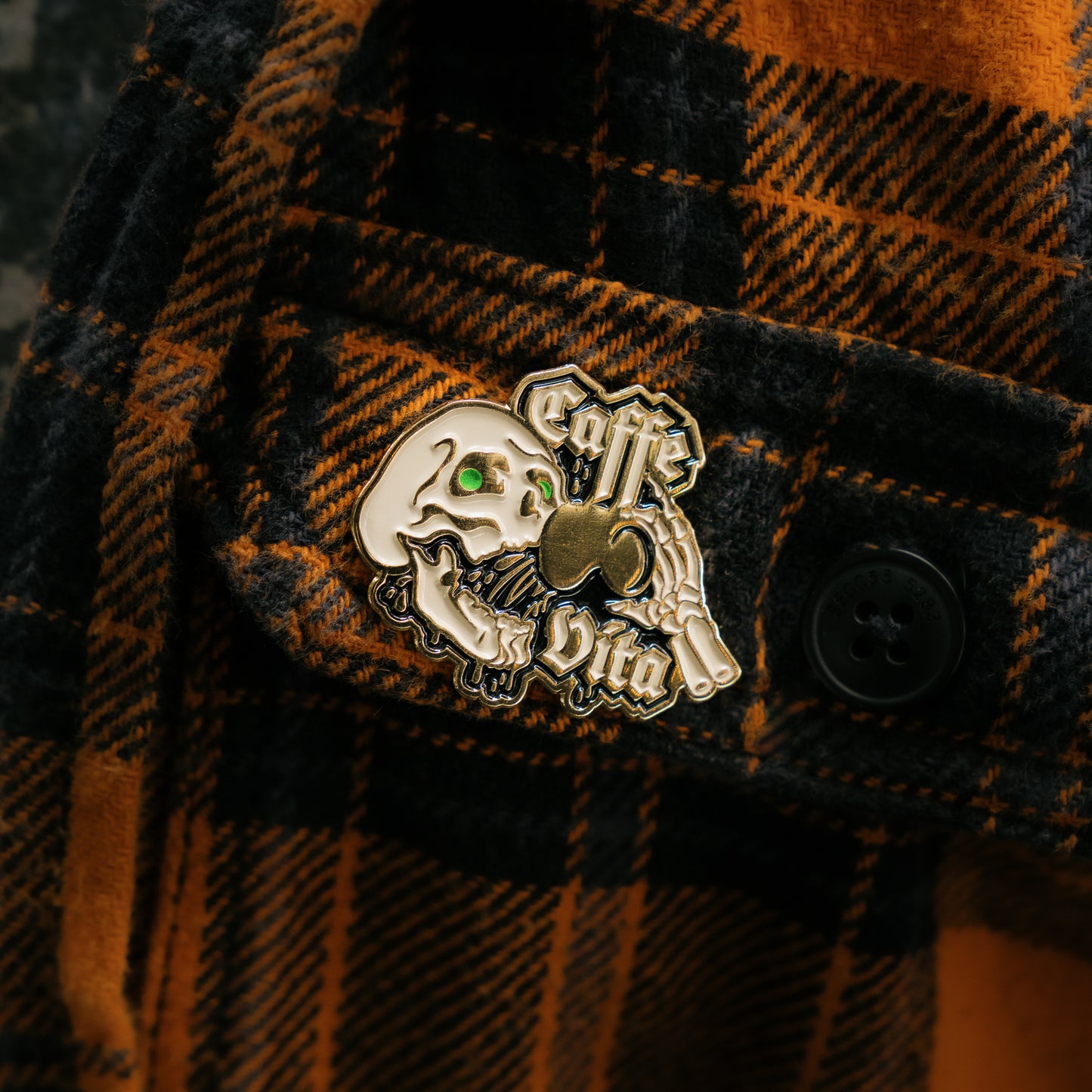 Close up detail, Skull enamel pin attached to plaid shirt pocket.