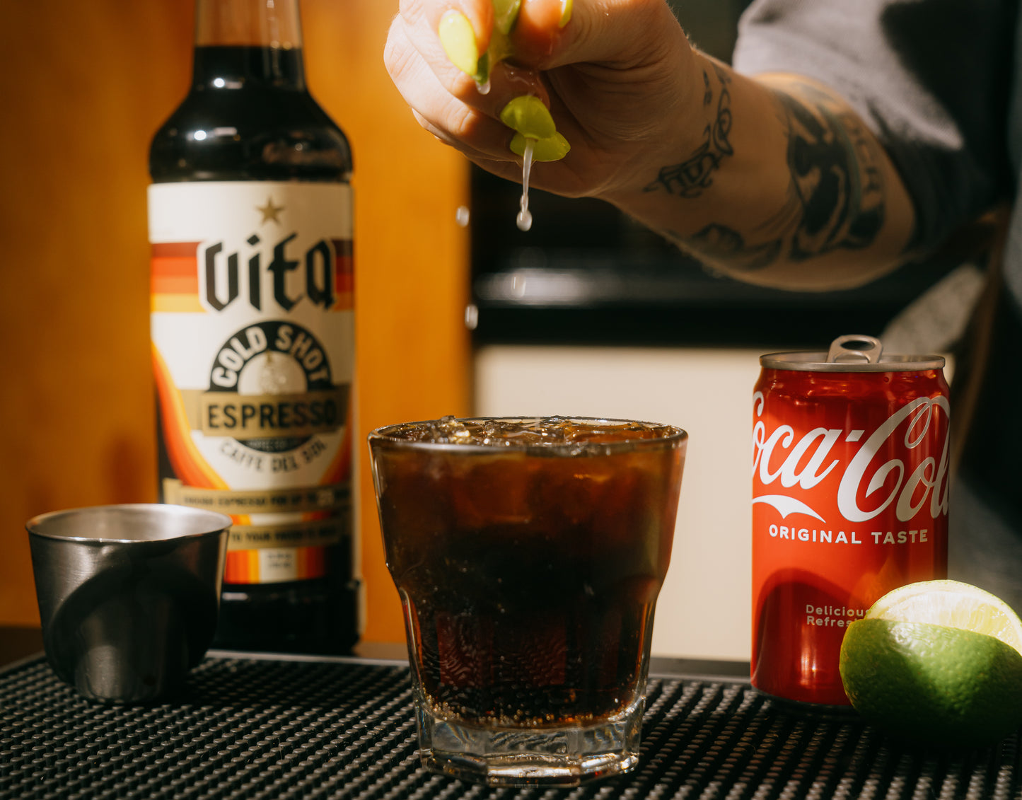 Cold Shot bottle with hand squeezing lime wedge over Cold Shot Coke in glass with cola can and lime.